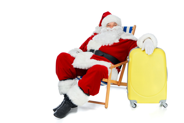 bärtige Weihnachtsmänner relaxen im Strandkorb mit gelber Reisetasche isoliert auf weißem Grund - Foto, Bild