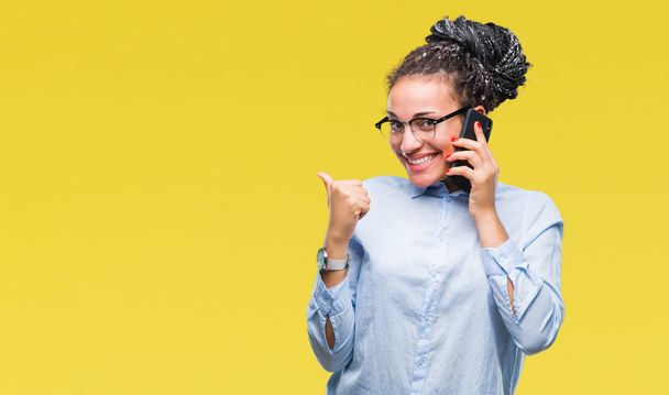 Μικρά πλεκτά μαλλιά αφρικανική αμερικανική επιχείρηση κορίτσι δείχνει κλήσεις χρησιμοποιώντας smartphone μέσω απομονωμένη υπόβαθρο ευτυχισμένη με μεγάλο χαμόγελο κάνει εντάξει σήμα, τον αντίχειρα επάνω με τα δάχτυλα, καλό σημάδι - Φωτογραφία, εικόνα