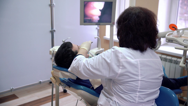 Жінка-стоматолог вивчає зуби пацієнта з внутрішньо-оральною камерою і показує результати на моніторі. Лікування та профілактика стоматологічних захворювань, карієсу, концепції здоров'я
. - Кадри, відео