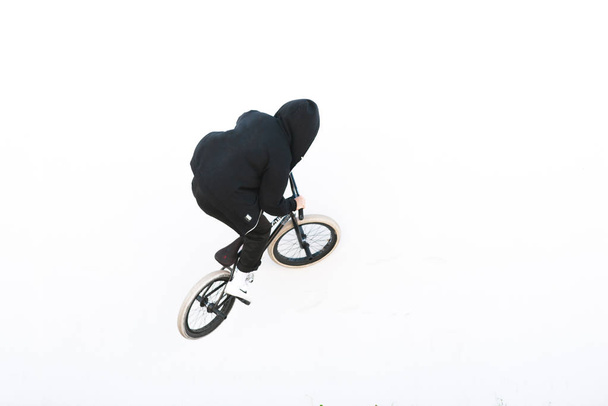 O cavaleiro está de volta em roupas escuras montando uma parede branca em uma bicicleta bmx. bmx truque em um fundo branco. Espaço de cópia
 - Foto, Imagem