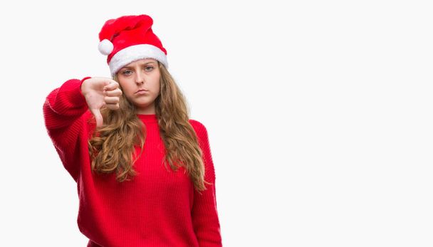 Jonge blonde vrouw met kerstman hoed met boos gezicht, minteken weergegeven: afkeer met duimen naar beneden, afwijzing concept - Foto, afbeelding