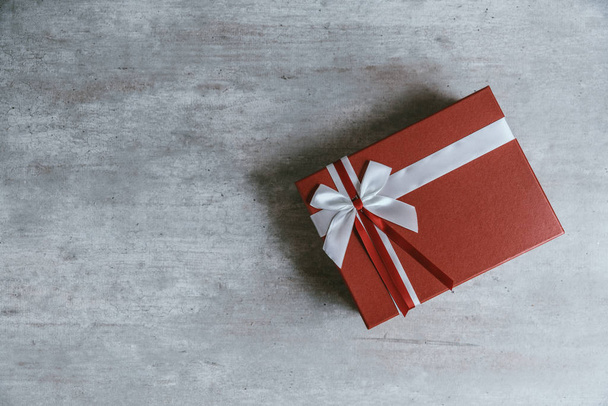 Ručně vyráběné vánoční dárek nebo červené krabičce zabalený v sulfátového papíru s bílou mašlí na dřevěné pozadí. Pohled shora, plochý ležel, kopie prostor. Blahopřání. - Fotografie, Obrázek