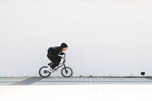 Bmx rider in casual clothing rides a bicycle on the background of a white wall. Bmx concept. Street freestyle on bmx - Foto, Imagen