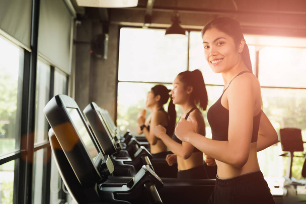 Mujer asiática feliz con grupo de jóvenes corriendo o trotando en cintas de correr en el gimnasio deportivo moderno. ejercicio y concepto deportivo
. - Foto, Imagen