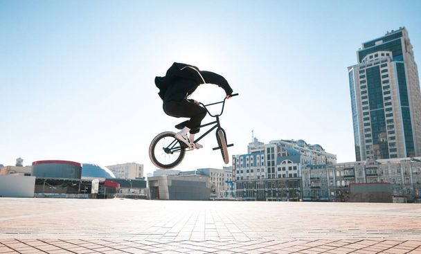 Silueta bmx Rider, skákání na pozadí slunce a městské krajiny za jasného letního dne. BMX cyklista dělá složité triky na kole - Fotografie, Obrázek