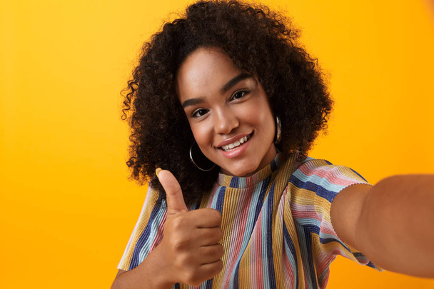 Image of beautiful young happy african cute girl posing isolated over yellow background take a selfie with thumbs up gesture. - Foto, imagen