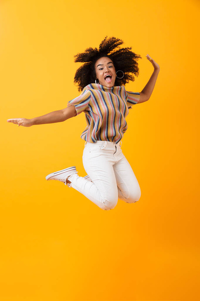 Image of emotional pretty african woman jumping isolated over yellow background. - Foto, imagen