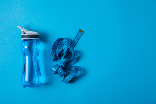 top view of sport bottle and measuring tape isolated on blue, minimalistic concept  - Photo, Image
