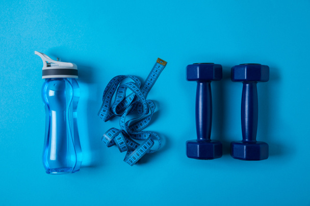 view from above of sport bottle with water, measuring tape and dumbbells isolated on blue  - Photo, Image