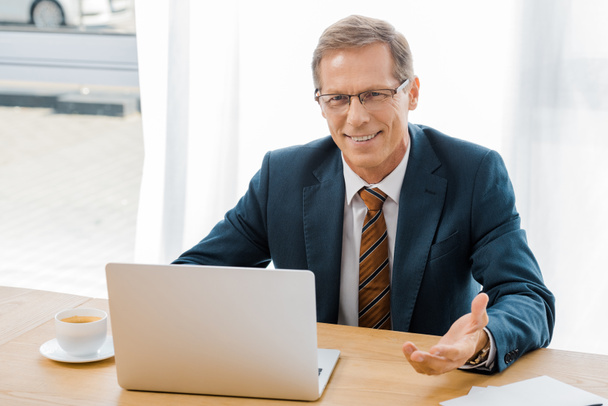 adulte souriant homme dans des lunettes assis à table avec ordinateur portable dans le bureau d'assurance
 - Photo, image