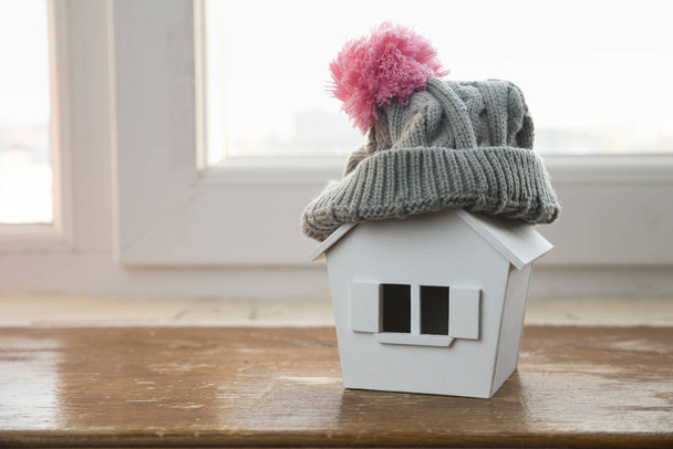 casa no inverno - conceito de sistema de aquecimento e tempo nevado frio com modelo de uma casa usando um boné de malha
 - Foto, Imagem