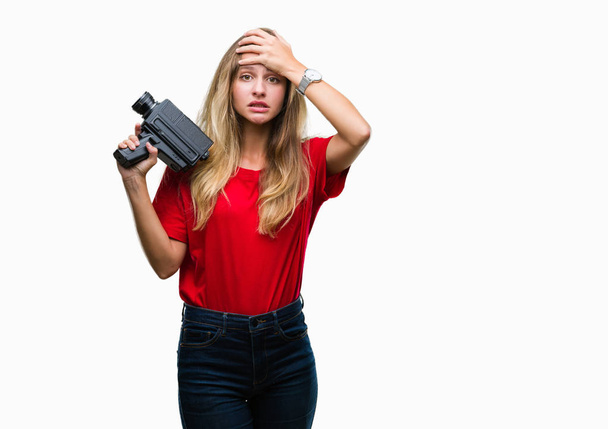 Young beautiful blonde woman filming using vintage camera over isolated background stressed with hand on head, shocked with shame and surprise face, angry and frustrated. Fear and upset for mistake. - Foto, Imagem