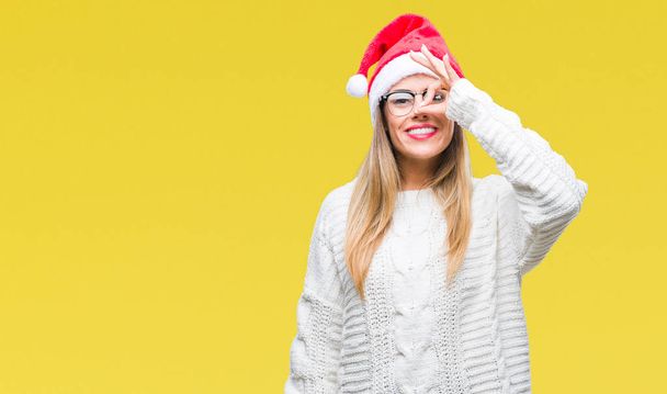 Nuori kaunis nainen yllään joulu hattu yli eristetty tausta tekee ok ele käsin hymyillen, silmä katselee sormien läpi onnellinen kasvot
. - Valokuva, kuva