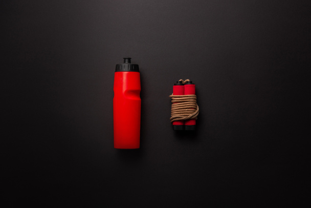 vlakke leggen met rode sport fles en springtouw geïsoleerd op zwart, minimalistische concept  - Foto, afbeelding