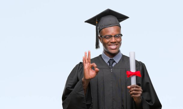 Young graduated african american man holding degree over isolated background doing ok sign with fingers, excellent symbol - Photo, image