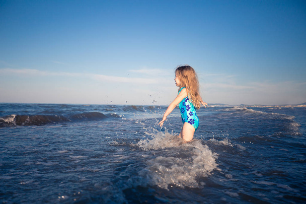 Summer background. Little girl in blue swimsuit standing in blue sea. Happy child on holidays. - Foto, Imagen