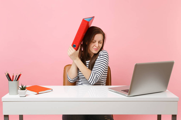 Upset woman defending hiding behind red folder with paper document work on project while sit at office with laptop isolated on pastel pink background. Achievement business career concept. Copy space - Photo, Image