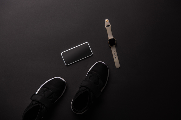 view from above of smartphone, smartwatch and sneakers isolated on black - Foto, afbeelding