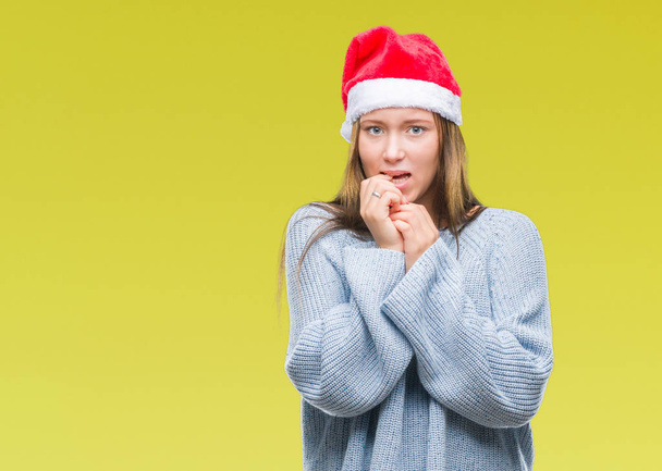 Νέοι όμορφη καυκάσιος γυναίκα φοράει καπέλο Χριστουγέννων πέρα από το απομονωμένο υπόβαθρο ψάχνει αγχωμένοι και νευρικοί με τα χέρια στο στόμα δάγκωμα νύχια. Πρόβλημα του άγχους. - Φωτογραφία, εικόνα