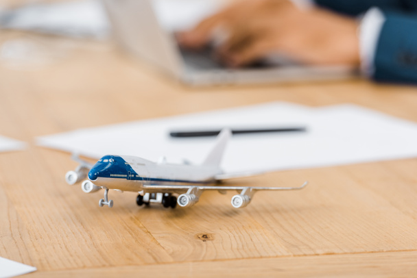 背景をぼかした写真のラップトップを使用してオフィス ワーカーと木製のテーブルでおもちゃの飛行機  - 写真・画像