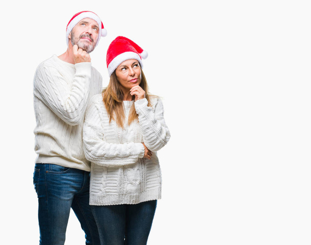 Середньовіччя іспаномовна пара носить різдвяний капелюх над ізольованим тлом з рукою на підборідді, думаючи про питання, стомлююче вираження. Посміхаючись з розсудливим обличчям. Концепція сумніву
. - Фото, зображення