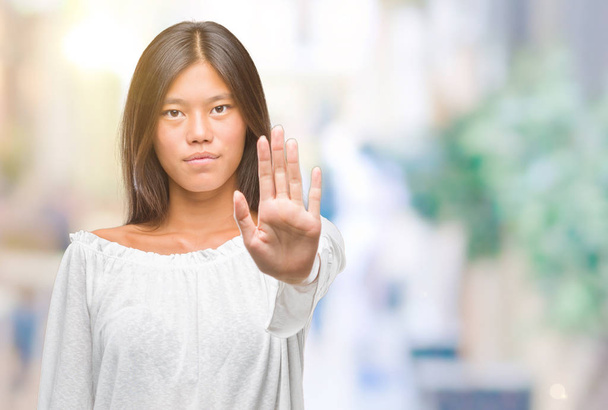 Joven mujer asiática sobre fondo aislado haciendo dejar de cantar con la palma de la mano. Expresión de advertencia con gesto negativo y serio en la cara
. - Foto, imagen