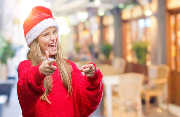 junges schönes Mädchen, das Weihnachtsmütze über isoliertem Hintergrund trägt und mit dem Finger in die Kamera zeigt, mit fröhlichem und lustigem Gesicht. gute Energie und Stimmung. - Foto, Bild