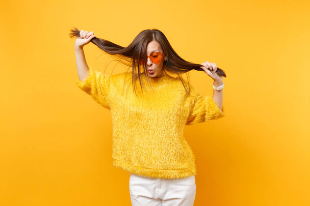 Pretty young woman in fur sweater, heart orange glasses fool around, holding her hair like ponytails isolated on bright yellow background. People sincere emotions, lifestyle concept. Advertising area - Φωτογραφία, εικόνα