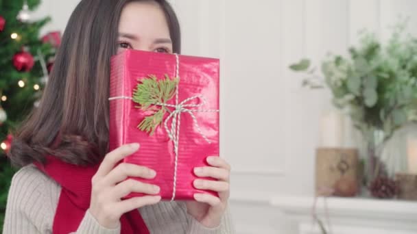 Cheerful happy young Asian woman holding christmas gifts smiling to camera in her living room at home in Christmas Festival. Lifestyle woman celebrate Christmas and New year concept. - Materiał filmowy, wideo