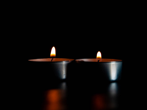 Δύο αναμμένα κεριά με μια πορτοκαλί φλόγα και απομονωμένη σε ένα μαύρο φόντο - Φωτογραφία, εικόνα