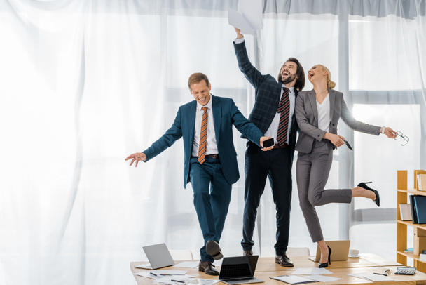 trabalhadores de seguros alegres dançando na mesa e jogando papéis na reunião no escritório
 - Foto, Imagem