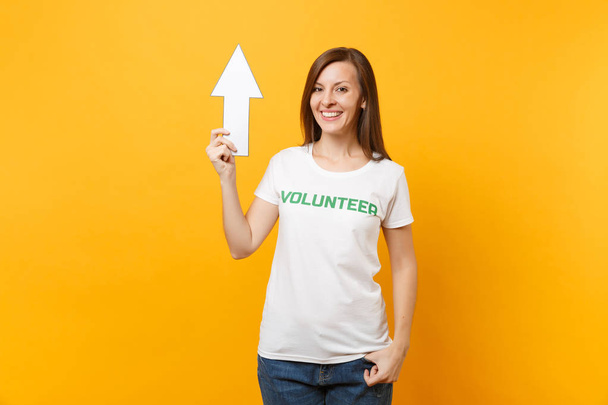 Porträt einer glücklichen Frau in weißem T-Shirt mit Schriftzug Grüner Titel Ehrenamtlicher Pfeil zeigt vereinzelt nach oben auf gelbem Hintergrund. Freiwillige kostenlose Hilfe hilft Wohltätigkeitsorganisation Gnade Arbeit Konzept - Foto, Bild