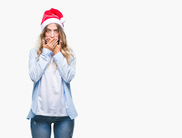 Krásná mladá blond žena nosí vánoční čepice izolované pozadí šokován, pokrývající ústa rukama za chybu. Tajné koncept. - Fotografie, Obrázek