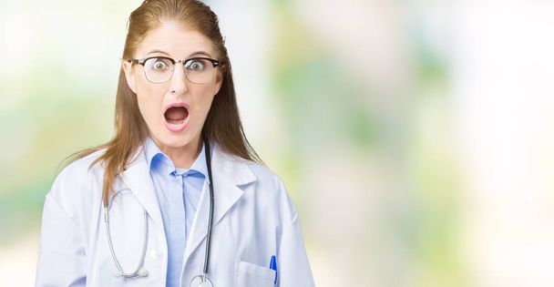 Moyen âge mature médecin femme portant un manteau médical sur fond isolé Dans le visage de choc, l'air sceptique et sarcastique, surpris par la bouche ouverte
 - Photo, image