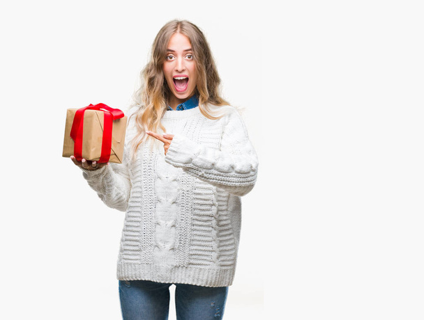 schöne junge blonde Frau hält Geschenk über isolierten Hintergrund sehr glücklich zeigt mit der Hand und dem Finger - Foto, Bild