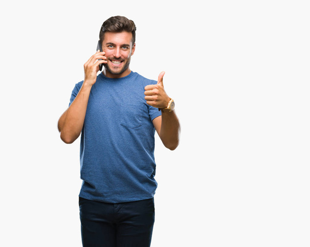 Młody przystojny mężczyzna rozmowa na smartphone na białym tle szczęśliwy z uśmiechem robi znak ok, kciuk palcami, bardzo dobry znak - Zdjęcie, obraz