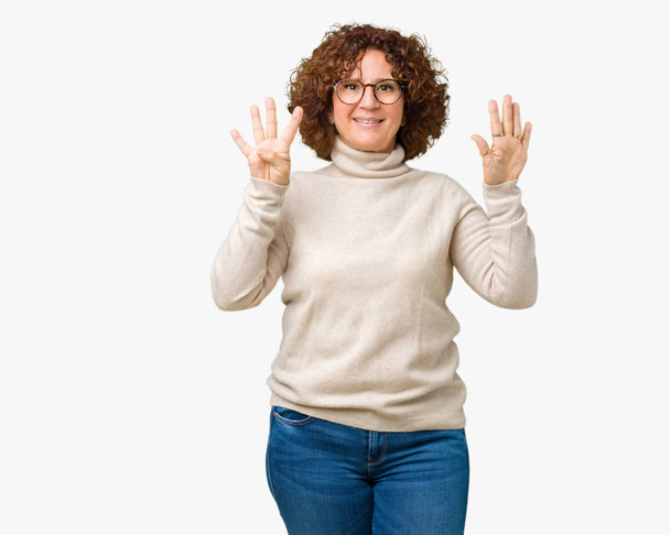 孤立した背景表示と指で上向きにタートルネックのセーターとメガネを着て美しい中間エイガー年配の女性ナンバー ナイン自信を持って、幸せな笑みを浮かべて、. - 写真・画像