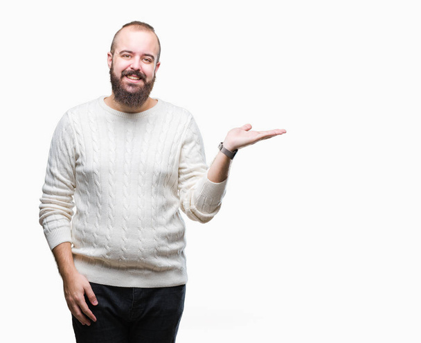 Young caucasian hipster man wearing winter sweater over isolated background smiling cheerful presenting and pointing with palm of hand looking at the camera. - Foto, Imagen