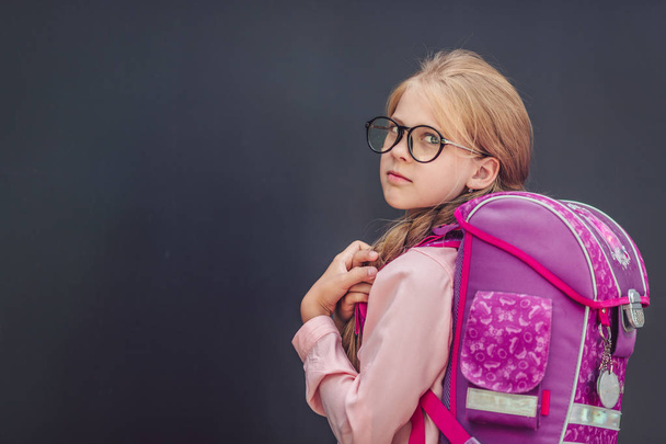 Little schoolgirl with a backpack on a black background - Photo, Image