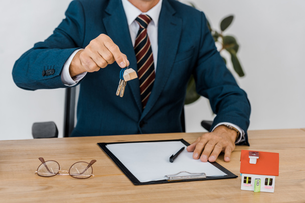 insurance agent holding keys with house model and glasses on table - Photo, Image