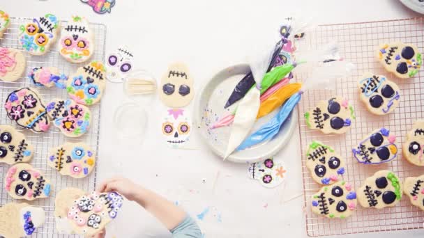 Menina decorando biscoitos de crânio de açúcar com gelo real para o feriado Dia de los Muertos
. - Filmagem, Vídeo
