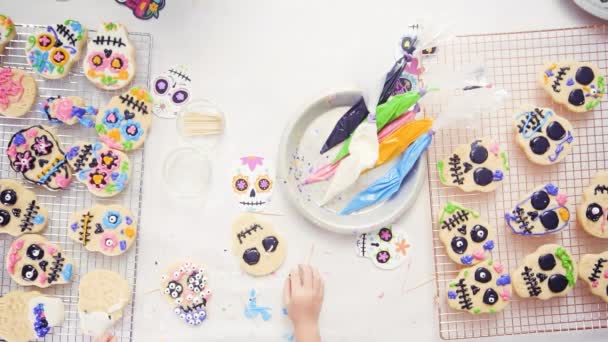 Menina decorando biscoitos de crânio de açúcar com gelo real para o feriado Dia de los Muertos
. - Filmagem, Vídeo