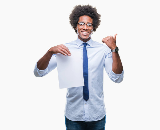 Afro american man holding blank paper contract over isolated background pointing and showing with thumb up to the side with happy face smiling - 写真・画像