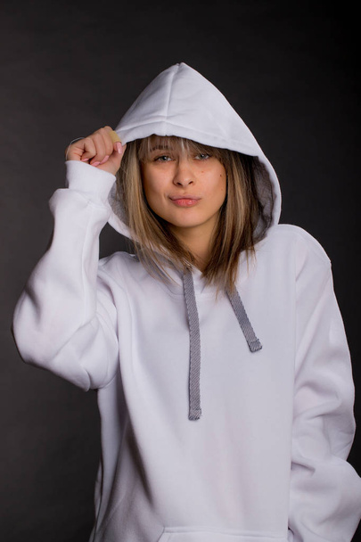 Beautiful young woman in a large white hooded sweatshirt. Studio portrait on black background - Foto, Imagem