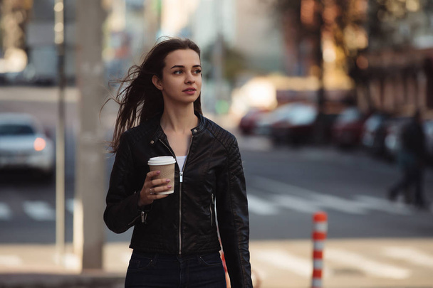 Beautiful woman holding paper coffee cup and enjoying a walk in the city - Photo, image