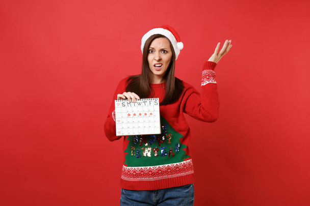 Спантеличені Санта дівчинка тримає жінок періодів календар для перевірки дні менструації, ізольовані на червоному тлі. Медичні healthcare гінекологічних. Щасливого нового року 2019 святкування свято партії концепції - Фото, зображення