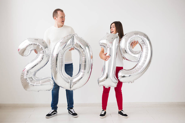 Conceito de ano novo, celebração e feriados - Sinal de posse de casal de amor surpreso 2019 feito de balões de prata para o ano novo no fundo da sala branca
 - Foto, Imagem