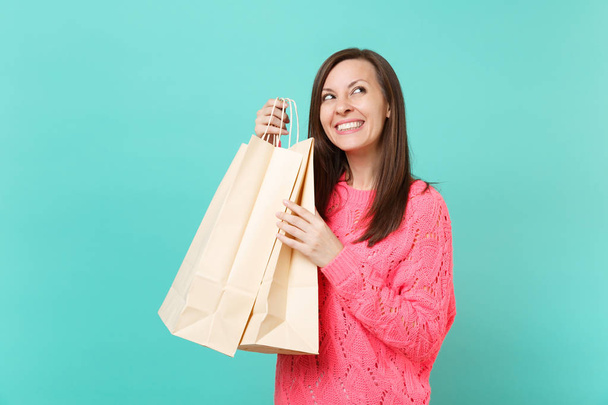 Giovane donna sognante in maglia rosa maglione guardando in alto, tenendo pacchetti borse con acquisti dopo lo shopping isolato su sfondo blu parete turchese. Concetto di stile di vita. Falsificare spazio di copia
 - Foto, immagini
