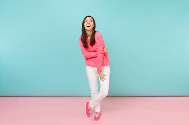 Полный портрет улыбающейся девушки в трикотажном розовом свитере, белые брюки позируют изолированно на ярко-розовом голубом пастельном фоне в студии. Концепция модного образа жизни. Пространство для копирования
 - Фото, изображение