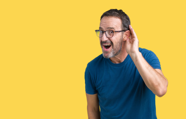 Brunetě středního věku otřepané starší muž wearin brýle izolované pozadí s úsměvem s rukou přes ucho naslouchá slyšení zvěsti nebo drby. Hluchota koncept. - Fotografie, Obrázek